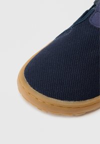 Μπλε ναυτικό πάνινο παπούτσι με υφή στην επιφάνεια, στρογγυλεμένη μύτη και αντίθετη καφέ ελαστική σόλα. Ραφές κατά μήκος της άκρης.