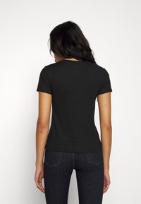 T-shirt nera a maniche corte con scollo rotondo e silhouette aderente, realizzata in morbido tessuto di cotone, abbinata a jeans in denim scuri.