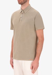 Polo beige a maniche corte con colletto, patta con tre bottoni e cuciture decorative arancioni all'orlo. Materiale in cotone, texture liscia.