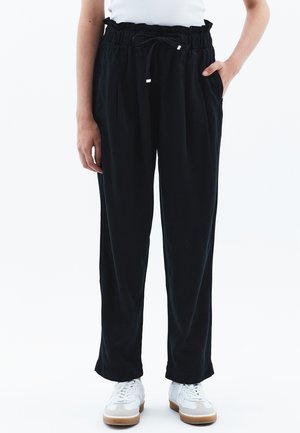 Sorte, løstsiddende bukser med elastisk talje og snor. Har sidelommer og manchetter ved anklerne. Bæres med hvide sneakers.