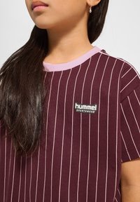 Burgundy t-shirt med kort ärm och vertikala ljusrosa ränder. Har en rund halsringning med en ljusrosa kant och en "hummel" logotypplätt.