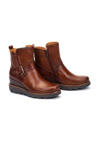 Bottines en cuir marron à fermeture éclair sur le côté, avec une accent de boucle et une semelle en wedge texturée. Présente des détails de couture le long de la tige.