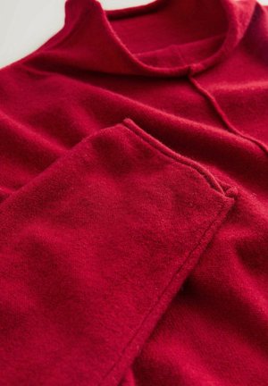 Roter Wollpullover mit einer weichen Textur, ausgestattet mit einem einfachen Kragen und einer Tasche am Ärmel. Der Stoff wirkt warm und gemütlich.