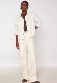 Giacca oversize beige chiaro con Bottoni neri, abbinata a un top marrone scuro e pantaloni a sbuffo color crema. Tessuto liscio con dettagli di cucitura minimi.