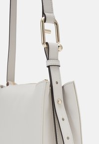 Borsa a tracolla in pelle grigia chiara con hardware dorato, tracolla regolabile e dettagli di cucitura, apertura superiore e chiusura con zip.