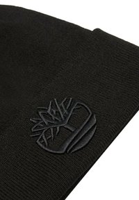 Beanie nero lavorato a maglia con tessuto testurizzato e logo ricamato in rilievo di un albero all'interno di un cerchio, posizionato vicino al bordo.