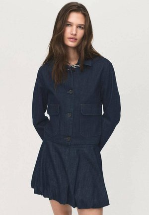 Veste en denim foncé avec deux poches avant, dotée d'un col et d'une fermeture à boutons, associée à une jupe en denim évasée.