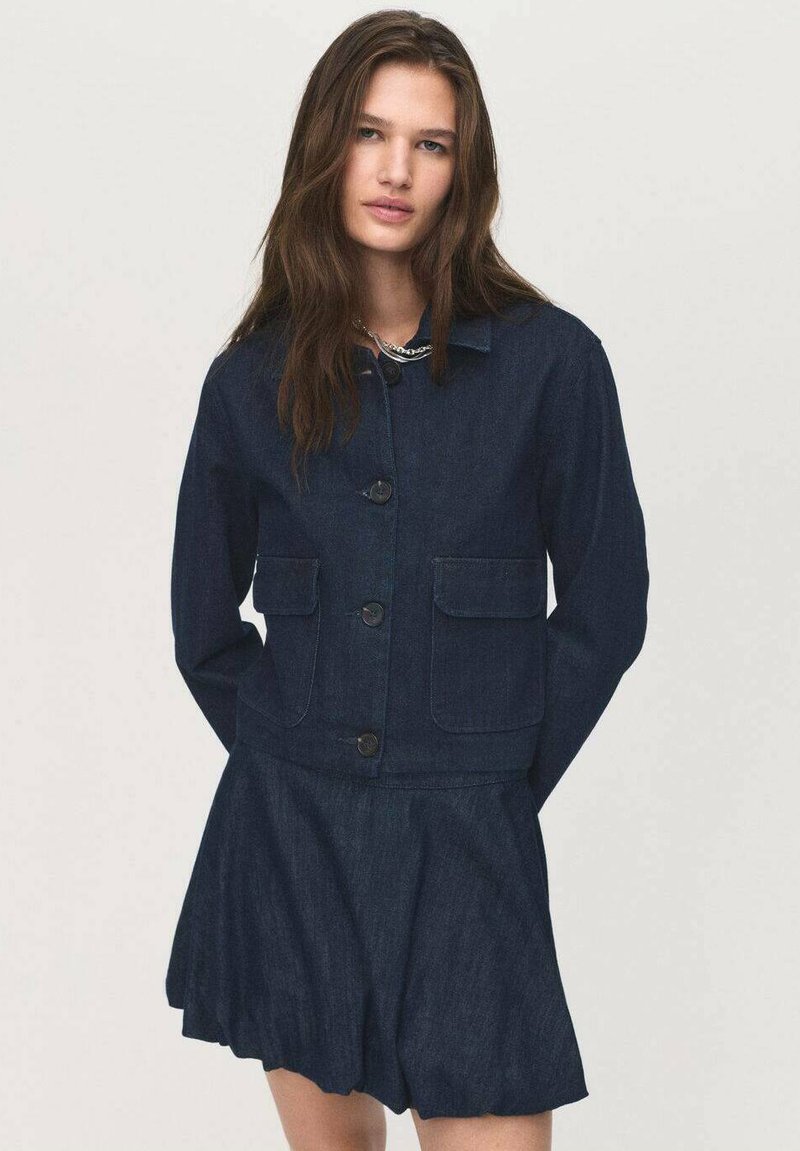 Temna denim jakna z dvema sprednjima žepoma, s kragnatim ovratnikom in gumbom za zapiranje, v kombinaciji z razširjenim denim krilom.