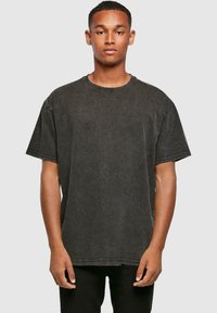 T-shirt noir oversize en tissu doux avec un col rond, des manches courtes et des détails de couture visibles. Présente une coupe décontractée.