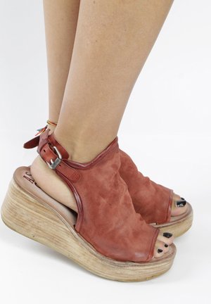 Sandales compensées en daim rouge avec design à bout ouvert, bride à la cheville et plateforme en bois texturé. Présentent une forme arrondie et des ferrures polies.