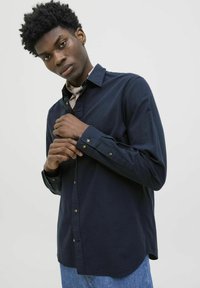 Navyblauwe button-up shirt met lange mouwen, een pointe kraag en messing knopen. Gecombineerd met een lichtgekleurde sjaal en denim jeans.