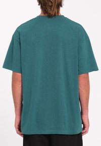 T-shirt di cotone color teal, maniche corte, vestibilità relax, collo rotondo, modello tinta unita, superficie liscia, senza loghi o grafiche visibili.