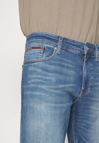 Jeans in denim blu con un lavaggio chiaro, caratterizzati da un classico design a cinque tasche e una cucitura decorativa in rosso, bianco e giallo sulla tasca posteriore.