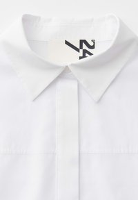 Weißes Hemd mit Kragen, Vorderansicht, spitzer Kragen und teilweise sichtbare Größenetikett mit der Aufschrift "24" im Nackenbereich.