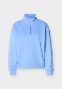 Pull bleu clair à manches longues avec col montant, fermeture éclair devant sur la moitié, poignets et bas côtelés, et petit logo sur le côté gauche de la poitrine.