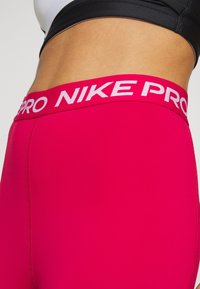 Legginsy Nike Pro w intensywnym różowym kolorze, z szerokim białym pasem w talii z logo, gładką teksturą i dopasowanym krojem.