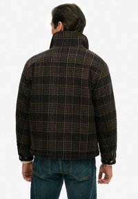 Sort og brunt ternet jakke med høj krave, tekstureret stof og knapmanchetter. Bæres over blå denim, set fra ryggen.