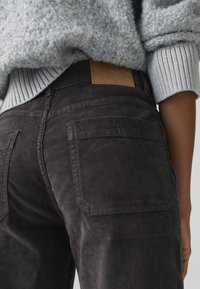 Dark gray corduroy pants with two back pockets. Features a brown leather patch at the waist. Soft texture and ribbed pattern visible.