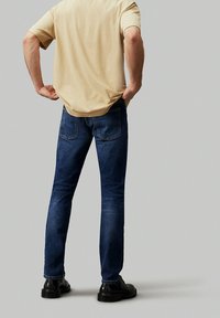 Mörkblå denimjeans med smal passform, med två bakfickor, kombinerade med en beige kortärmad skjorta och svarta skor.