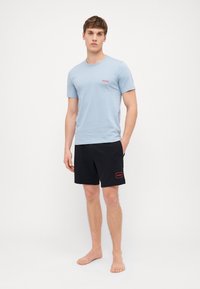 Light blue cotton t-shirt with red "HUGO" logo, paired with black shorts featuring red logo patch. Simple, casual design, relaxed fit.