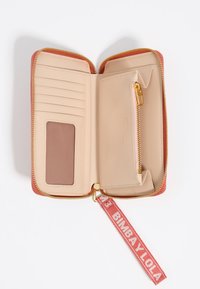 Cartera con cremallera en cuero rosa y beige, que presenta ranuras para tarjetas, un bolsillo transparente para identificación y un tirador de cremallera dorado. Incluye una correa de tela para la muñeca.