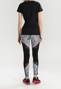 Czarny sportowy t-shirt z krótkimi rękawami, w zestawie z legginsami w wzory, posiadającymi siateczkowe wstawki i mieszankę kolorów szaro-czarnych.