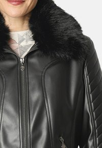 Mujer vestida con una chaqueta de cuero negra con mangas acolchadas en diagonal y un suave collar de piel negra, sobre una blusa de color claro con estampado.