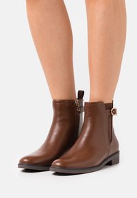 Brown leather ankle boots with a smooth finish, side zipper closure, elastic panel, and small decorative buckle on the side. Flat heel.
