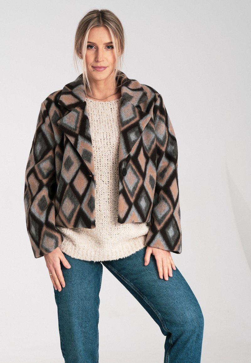 Gekürzte, gemusterte Jacke mit einem Diamantdesign in Braun-, Grau- und Schwarztönen. Verfügt über einen breiten Kragen und einen Knopfverschluss, kombiniert mit einem cremefarbenen Pullover.