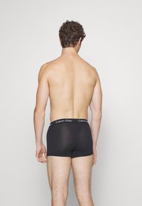 Boxer briefs neri in cotone con una vita elastica logo, mostrati da dietro su un torso nudo, trama liscia, design aderente.