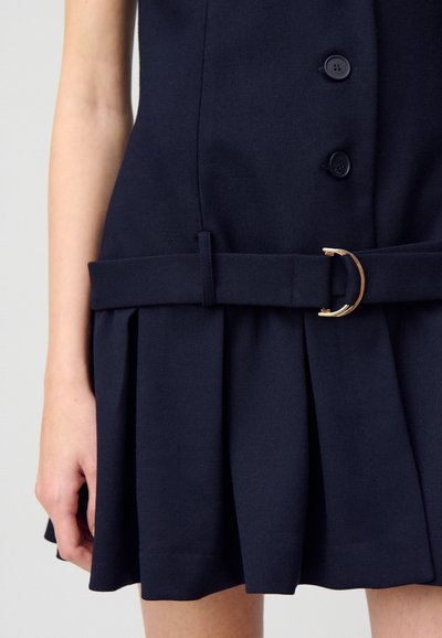 Robe bleu marine avec un corsage ajusté, des détails de boutons, une jupe plissée et une ceinture avec une boucle circulaire dorée. Fabriquée en tissu texturé.