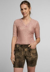 Rosa Spitzenbluse mit kurzen Ärmeln und V-Ausschnitt, kombiniert mit braunen Leder-Shorts, die mit floralen Stickereien und dekorativen Knöpfen versehen sind.
