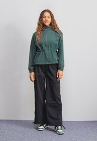 Grön zip-up jacka med åtdragen midja, i kombination med lösa svarta cargobyxor med fickor. Bärs med gröna och vita sneakers.