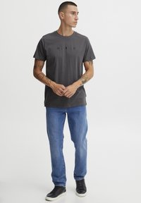 Grå t-skjorte med rund hals og "A.R.C." trykt i svart, sammen med blå denimbukser og svarte lavtopp sneakers.