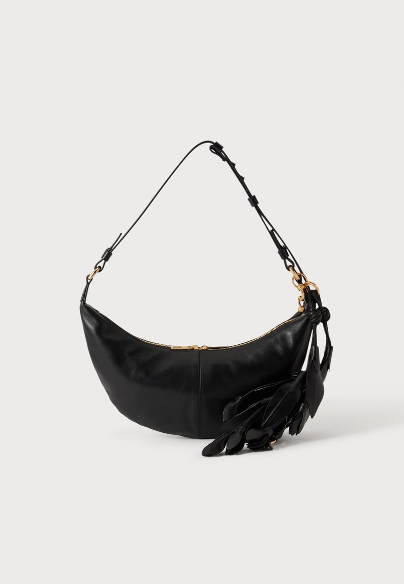 Sac d'épaule en cuir noir en forme de croissant avec bandoulière réglable, fermeture éclair dorée et pompons en cuir décoratifs en forme de feuille sur un côté.