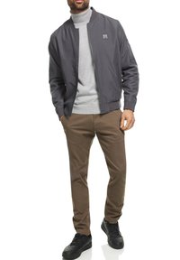 Grijze bomberjack met geribde kraag, gecombineerd met een lichtgrijze coltrui en bruine broek, aangevuld met zwarte sneakers.