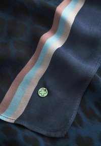 Foulard en soie de couleur bleu marine foncé avec un imprimé léopard. Il présente une surface texturée, des rayures horizontales multicolores en rose et bleu, et un accent logo vert.