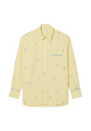 Camisa amarilla abotonada con finas rayas verticales azules, pequeños estampados azules de jugadores de tenis, bolsillo en el pecho y parche con logo en el puño izquierdo.