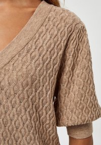 Beige pletený svetr s hlubokým V-výstřihem a krátkými rukávy. Obsahuje strukturovaný vlnitý vzor a žebrované manžety. Lehká tkanina.