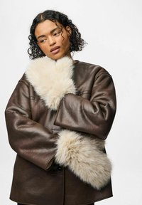 Brązowa skórzana kurtka o prostokątnej sylwetce i szerokich rękawach, z dużymi kremowymi mankietami z sztucznego futra, które dodają tekstury i ciepła.