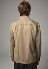Khaki jacket with a collared neckline, textured fabric, and button cuffs, shown from the back against a neutral background.