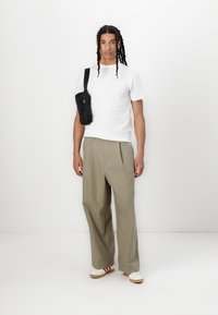 White t-shirt, loose khaki trousers, cream shoes with red stripes, and a small black crossbody bag with a zipper and strap.