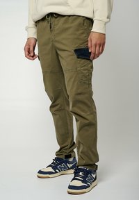 Pantalones cargo en algodón verde oliva, que cuentan con múltiples bolsillos, incluido un bolsillo parche con acentos de mezclilla, y un ajuste ceñido en los tobillos.