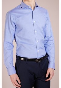 Camicia da uomo a maniche lunghe di colore azzurro, con motivo a quadri, colletto button-down e bottoni bianchi, abbinata a pantaloni blu navy e una cintura nera.