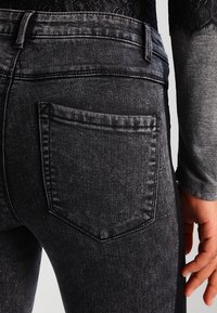 Vaqueros de mezclilla negros con corte ajustado, que cuentan con un bolsillo trasero, tejido texturizado y costuras de contraste. La cintura tiene trabillas para cinturón.