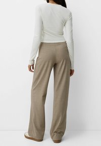 Bílý top s dlouhým rukávem a béžové kalhoty s širokými nohavicemi. Kalhoty mají jemný texturovaný vzor a uvolněný střih, navržené pro pohodlí.