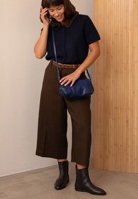 Maglione corto blu navy con colletto in pelliccia, pantaloni larghi marroni, cintura in pelle marrone e borsa blu navy. Stivali alla caviglia in pelle nera.