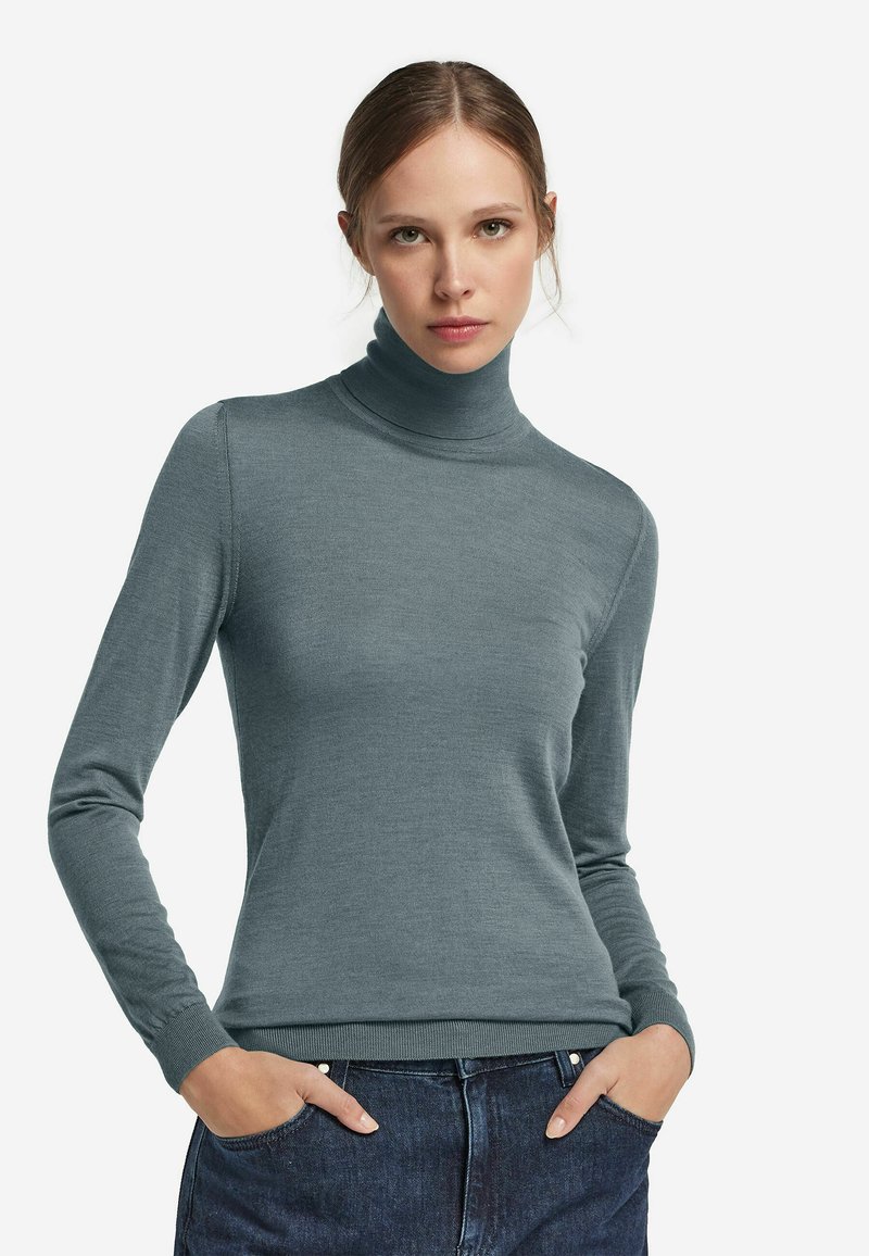 Enganliegender Rollkragenpullover aus weichem, strukturiertem Teal-Stoff. Lange Ärmel und gerippte Bündchen sowie Saum. Kombiniert mit dunklem Denim für einen Kontrast.
