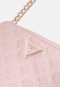 Bolso sintético de color rosa claro con patrones florales en relieve, correa de cadena en tono dorado y placa triangular con el logo "GUESS USA".
