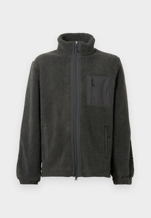 Chaqueta de forro polar gris oscuro con cremallera completa, cuello alzado, bolsillo en el pecho con cremallera, puños elásticos y dos bolsillos laterales sobre un fondo liso.